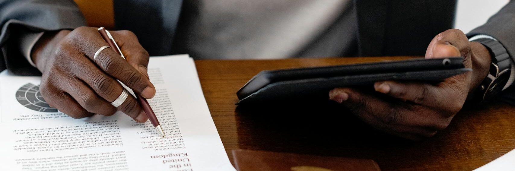Businessman in black suit working with documents and tablet at an office desk.