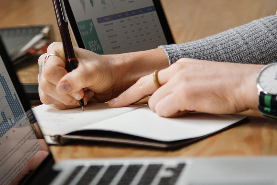 Person writing with laptops and spreadsheets