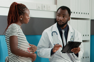 obstetrician using digital tablet consult patient male doctor and talking with woman with baby bump