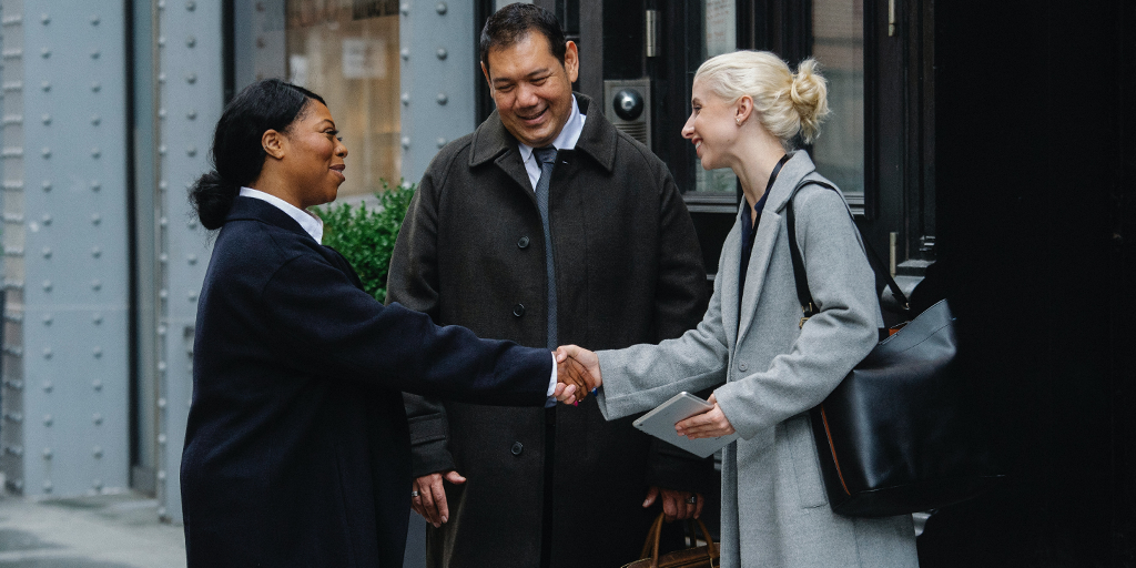 Two women meeting and shaking hands with a man standing between them